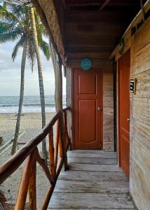 un pasillo de madera que conduce a la playa con una puerta roja en Palmarío Hostal en Guachaca