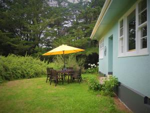 Tinui Food Forest Cottage في Whareama: طاولة وكراسي مع مظلة صفراء على ساحة