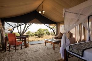 ein Schlafzimmer mit einem Bett und einem Schreibtisch in einem Zelt in der Unterkunft Serengeti Woodlands Camp in Serengeti-Savanne