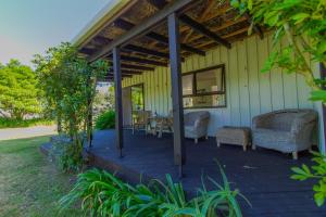 a patio with wicker chairs and tables on a house at Little Nikau - Tata Beach Holiday Home in Tata Beach