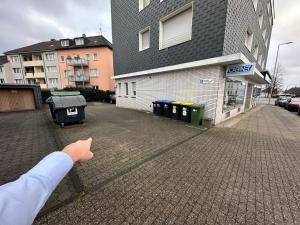 een hand van een persoon die wijst naar een gebouw met vuilnisbakken bij Moderne und gemütliches Appartement im EG mit eigenem Zugang in guter Wohnlage in Mülheim an der Ruhr