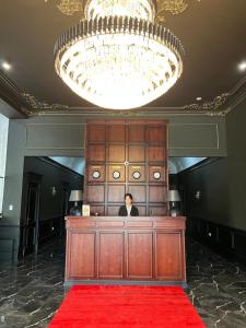 um homem de pé numa secretária num quarto com uma carpete vermelha em WIND HOTEL em Shymkent