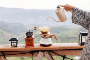 a woman holding a coffee maker and a blender on a table at At The Mountain Cottage, Tiny Home at Doichang with Hot tub Included Breakfast and Dinner in Ban Huai Khai