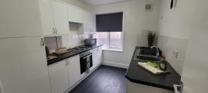 cocina con armarios blancos y encimera negra en Data House Holiday Apartment, en Atherstone