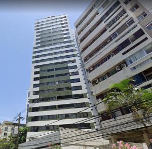 un edificio alto y blanco con árboles delante en Boa Viagem - Charmoso apartamento para casais, en Recife