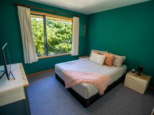 1 dormitorio con paredes verdes y 1 cama con ventana en Aorere House - Collingwood Holiday Home, en Collingwood