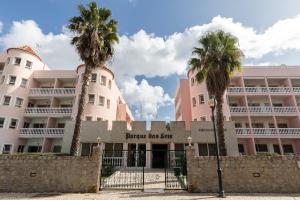 un edificio rosa con palmeras delante en Parque dos Reis Apartment, en Monte Gordo