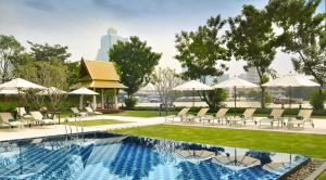 a swimming pool with chairs and umbrellas in a resort at Ibis Bangkok Riverside in Bangkok