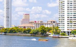 a boat on a river in a city with buildings at Ibis Bangkok Riverside in Bangkok