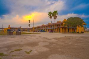 a yellow building with palm trees in a parking lot at OYO Hotel Kingsville - Hwy 77 in Kingsville