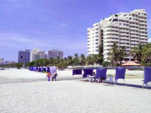 una playa con sombrillas azules y gente en la arena en HERMOSO Apartamento con piscina y cerca a PLAYA., en Santa Marta