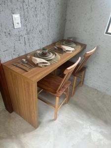 einem Holztisch mit 2 Stühlen und einem Tisch mit Tellern in der Unterkunft Nauru chalés milagres in São Miguel dos Milagres