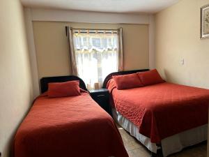 a bedroom with two beds with red sheets and a window at Apartamento #2 Portal de Occidente in Quetzaltenango