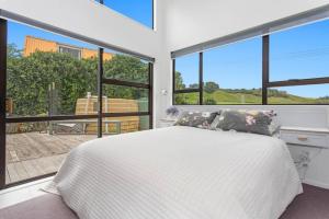 a bedroom with a white bed and large windows at Beach, Bikes and Bonfires in Opotiki