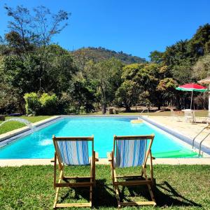 2 chaises assises en face d'une piscine dans l'établissement Pouso Donana Cama e Café, à Itaipava