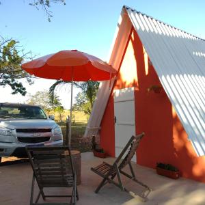 a patio with two chairs and an umbrella and a car at Camping e Pousada Buritis Park 