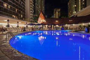 a large blue swimming pool in a city at night at OUTRIGGER Reef Waikiki Beach Resort in Honolulu