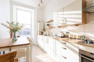 a kitchen with white cabinets and a table with a vase of flowers at GLASGOW WEST END 5 MIN WALK TO SECC AND HYDRO in Glasgow