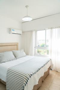 a white bedroom with a bed with a blue and white striped blanket at Departamento Laura con Cochera in Villa María