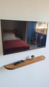 TV en una pared con dos mandos remotos en una estantería de madera en Espaço Zoey en Búzios