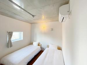 PRISM Inn Komagata Asakusa في طوكيو: سريرين في غرفة بجدران بيضاء