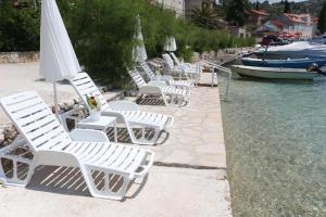 a row of white lawn chairs next to the water at Amare Apartments in Bobovišća