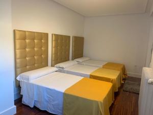 a room with three beds with yellow and white sheets at Villa Aurora in La Bañeza