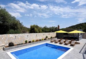 a swimming pool with chairs and a stone wall at Apartments Care in Okrug Donji