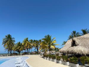 MoñitosHotel Bahia Rada的一个带椅子和棕榈树的海滩的度假酒店