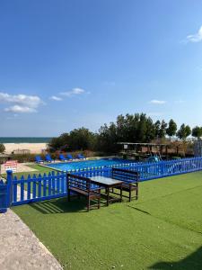 einem Picknicktisch und einer Bank neben einem blauen Zaun in der Unterkunft Al-Ashkhara Beach Resort منتجع شاطئ الأشخرة in Al Sharqiyah