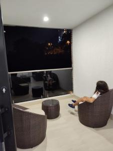 Ein Mädchen, das auf Stühlen in einem Raum mit einem großen Bildschirm sitzt in der Unterkunft Apartamento Amoblado en Manizales in Manizales