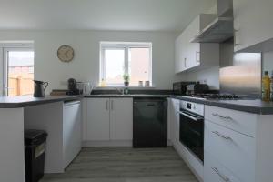 cocina con armarios blancos y lavavajillas negro en StayRight 4 Bedroom, 3 Bathroom House Near M4 - 15 mins to Cardiff & Newport, en Cardiff