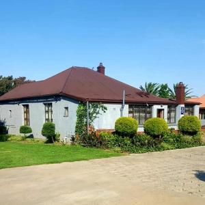 a white house with a red roof and bushes at Mthandi Wokuhamba Lodge in Dundee