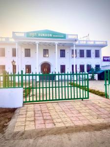 een wit gebouw met een groen hek ervoor bij Hotel Sukoon Bharatgarh in Rūpnagar