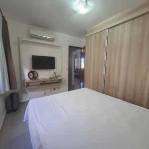 1 dormitorio con 1 cama blanca y TV de pantalla plana en Apartamento na Praia de Ponta Negra, en Natal