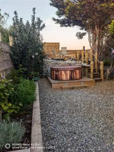 a garden with a wooden tub in the gravel at Brynglas Cottage with Hot Tub, Anglesey. in Llanfachraeth