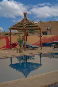 uma piscina com um gazebo, uma mesa e cadeiras em Auberge Les Roches em Merzouga