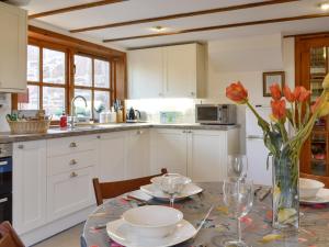 a kitchen with a table with red flowers in a vase at Willow Cottage in Kirriemuir