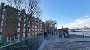 The Pearl of Greenwich - Two bedroom flat next to Cutty Sark في لندن: شخص يركب دراجة على الرصيف بجوار مبنى من الطوب