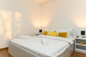 a white bedroom with a large bed with yellow pillows at JAD - Family Apartments & Studios in Braşov