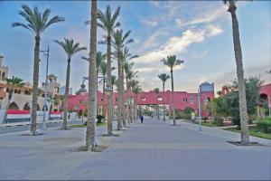 a street lined with palm trees and pink buildings at New cozy apt. on the promenade in Hurghada