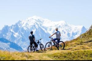 two men on bikes on a hill with a snow covered mountain at Chalet de L'Ours Blanc in Saint-Gervais-les-Bains
