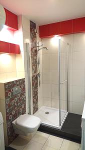 a bathroom with a toilet and a shower with red cabinets at Apartament Jantar 3B w Darłówku in Darłówko
