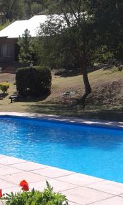 a blue swimming pool with a tree and a house at Los Cerezos in La Cumbre