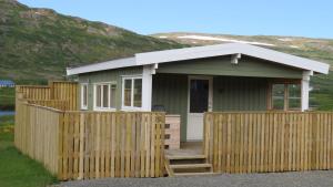 a small green cottage with a wooden fence at Hvammur 5 with private hot tub in Drangsnes
