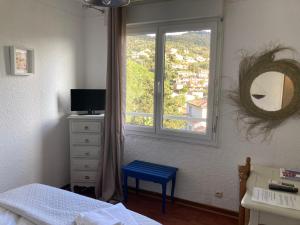a bedroom with a window and a bed with a blue stool at Hôtel Paradis in Bormes-les-Mimosas