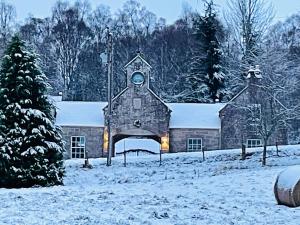 a large stone building with a clock tower in the snow at Coachmans Cottage in Aberlour