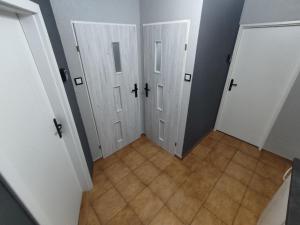 korytarz z 3 białymi drzwiami i podłogą wyłożoną kafelkami w obiekcie 3030 Jana Spychalskiego 32 - Tanie Pokoje w Apartamencie - samodzielne zameldowanie - self check in w Poznaniu