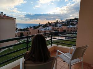 a woman sitting on a balcony looking out at the ocean at Garajau Terrace Adventure-Pool and Free Parking in Caniço