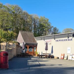 ein Restaurant mit Tischen und Sonnenschirmen an der Seite eines Gebäudes in der Unterkunft Watkin - Snowdon Cabins - cozy chalet - Glan Gwna, Caernarfon in Caeathro
